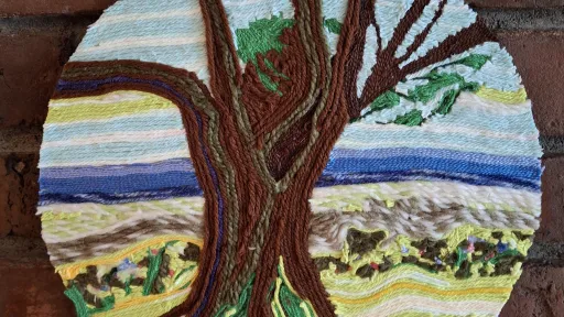 Woven tree in wool wall hanging with brown trunk and blue sky.